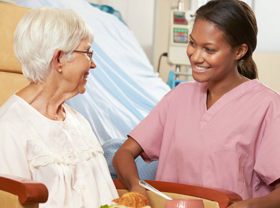Nurse serving meal to senior female patient sitting in chair